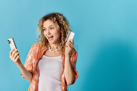 Woman with curly hair holding phone and credit card.