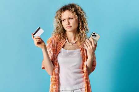 Eine Frau mit lockigem Haar hält Kreditkarte und Handy in der Hand.