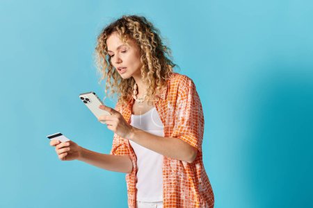 Woman with curly hair holds cell phone and credit card.