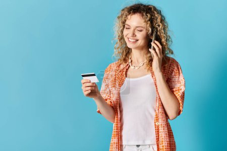 Young woman with curly hair holding credit card and talking on phone, all against vibrant backdrop.