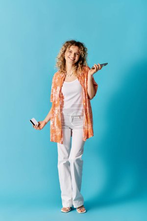 Curly-haired woman holding cell phone against blue background.