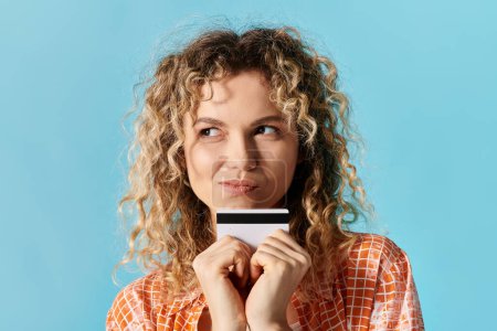 Junge Frau mit lockigem Haar hält selbstbewusst eine Kreditkarte in der Hand.