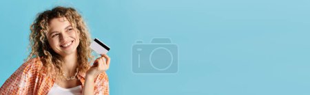 Photo for Young woman displaying credit card against blue background. - Royalty Free Image