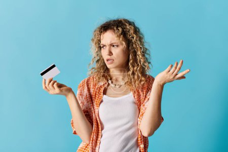 Una mujer elegante con el pelo rizado sosteniendo una tarjeta de crédito contra un telón de fondo vibrante.