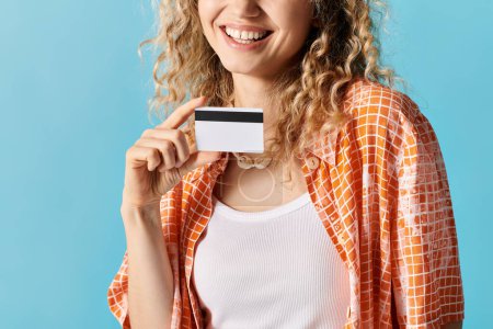 Woman with curly hair holding credit card on blue backdrop.