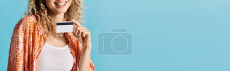 Téléchargez les photos : Une femme élégante tient gracieusement une carte de crédit sur un fond bleu vif. - en image libre de droit