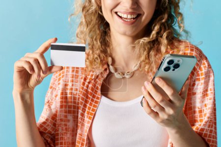 Woman holding credit card and phone in vibrant setting.