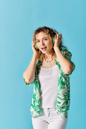 Curly-haired woman enjoys music with headphones on blue background.