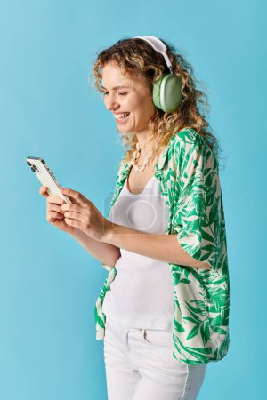Curly-haired woman wearing headphones, listening to music on her phone.