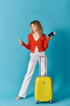 Foto de Stylish woman with yellow suitcase texting on phone - Imagen libre de derechos