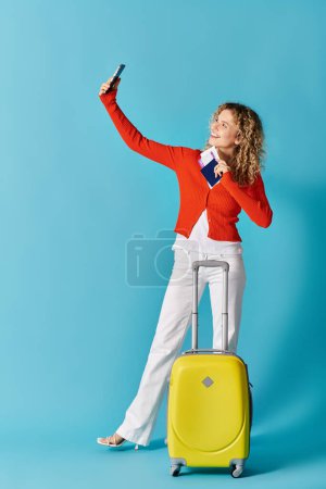 Curly-haired woman taking selfies with a yellow suitcase.