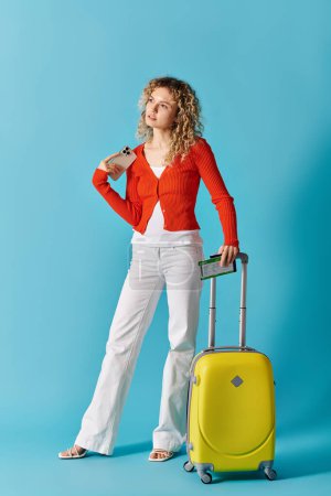 Une femme avec une valise jaune frappe une pose sur un fond bleu vif.