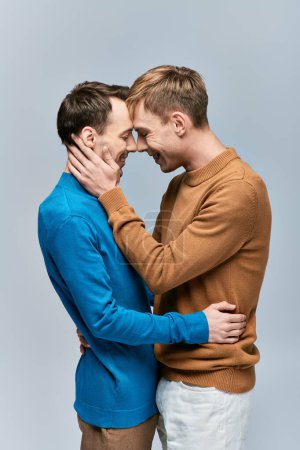 A loving gay couple in casual attire posing on a gray backdrop.