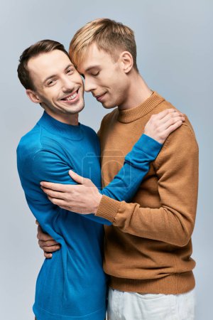 Foto de Dos hombres, una pareja gay cariñosa, abrazándose y sonriendo en un fondo gris. - Imagen libre de derechos