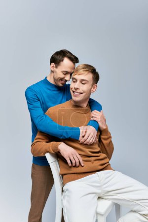 Photo for Two men sit on a chair, arms around each other, showcasing love and connection. - Royalty Free Image