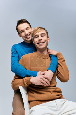 Two men in casual attire sitting on a chair, smiling warmly.