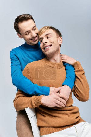 Téléchargez les photos : Deux hommes élégants, un couple gay aimant, s'assoient étroitement ensemble sur un fond gris. - en image libre de droit