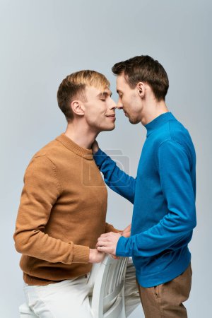 Two men in casual attire, lovingly touching noses against a gray backdrop.