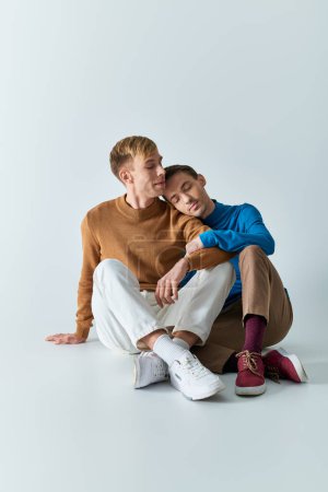 Casual gay couple happily pose on gray backdrop.