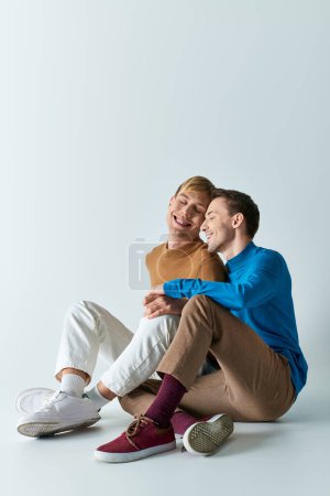 A loving gay couple in casual attire sitting on the ground, displaying affection.