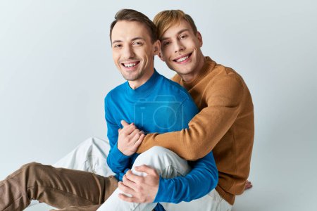 Two men in casual attire sit on the ground embracing each other gently.
