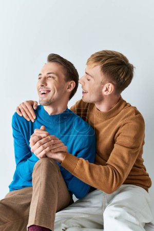 Photo for Two men in casual outfits, sitting on a bed, smiling warmly at each other. - Royalty Free Image