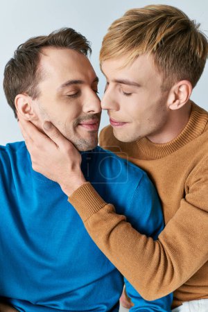 Photo for Two men in casual attire embracing each other tenderly against a gray backdrop. - Royalty Free Image