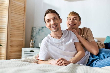 Foto de Dos hombres en atuendo casual disfrutando de tiempo de calidad juntos mientras están sentados en la parte superior de una cama. - Imagen libre de derechos