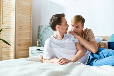 Foto de Una pareja gay amorosa con atuendo casual compartiendo un momento tierno mientras está sentada en una cama. - Imagen libre de derechos