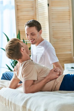 A man and his boyfriend share a tender moment while sitting on a bed.