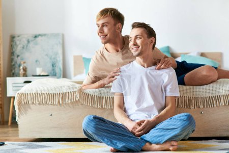 A couple of men in casual clothing sitting on top of a bed, enjoying each others company.