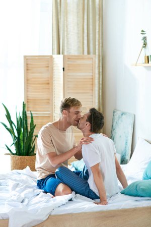 Téléchargez les photos : Un couple gay aimant en tenue décontractée partageant un baiser assis sur un lit. - en image libre de droit