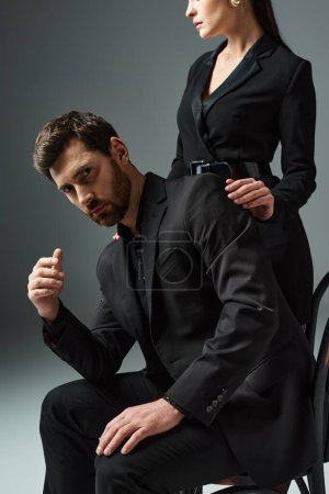 Foto de Un hombre y una mujer en traje elegante posan cerca de una silla juntos. - Imagen libre de derechos