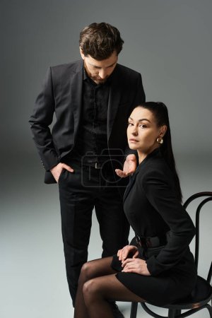 Un homme se tient à côté d'une femme en robe noire, à la fois élégant et captivant.