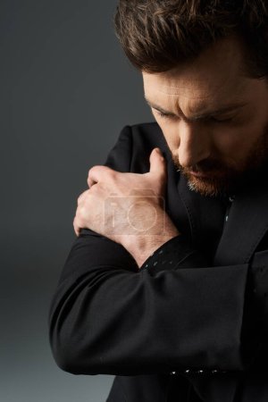Un hombre con un traje negro de pie con las manos juntas.