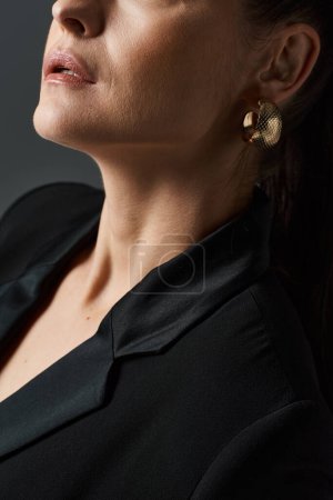 Eine Frau in schwarzem Hemd und schillernden goldenen Ohrringen posiert elegant.