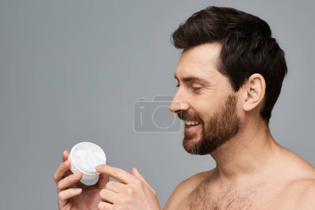 Foto de Hombre sin camisa sosteniendo una botella de crema con expresión enfocada. - Imagen libre de derechos