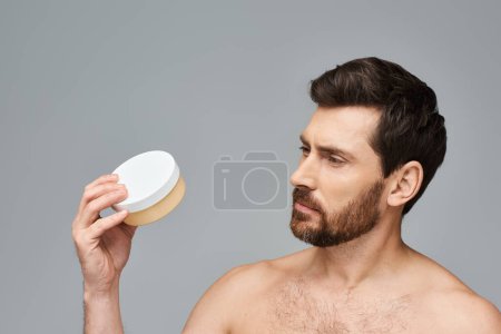 Foto de Hombre guapo sostiene un frasco de crema. - Imagen libre de derechos