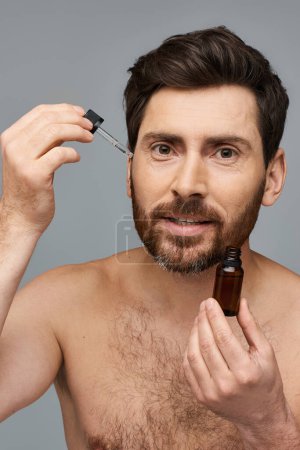 Téléchargez les photos : Homme barbu appliquant du sérum sur son visage. - en image libre de droit