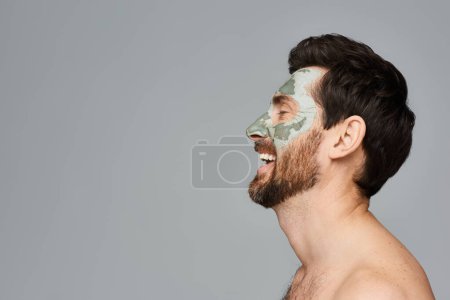 Foto de El hombre sin camisa exhibe una máscara facial, abrazando su rutina de cuidado de la piel. - Imagen libre de derechos