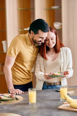 Una mujer pelirroja y un hombre barbudo se unen en una cocina moderna, disfrutando de un tiempo de calidad en casa.
