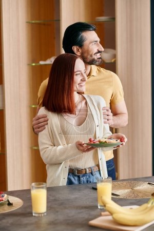 Foto de Una hermosa pareja de adultos, una mujer pelirroja y un hombre barbudo, de pie uno al lado del otro en una cocina moderna. - Imagen libre de derechos