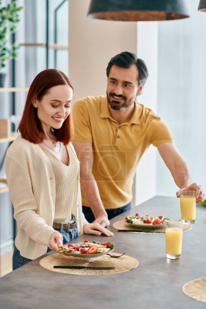 Ein schönes erwachsenes Paar, eine rothaarige Frau und ein bärtiger Mann, die in einer modernen Küche Essen zubereiten und die Zeit zu Hause gemeinsam genießen..