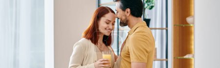 Foto de Una hermosa pareja de adultos, una pelirroja y un hombre barbudo, disfrutando de un vaso de jugo de naranja juntos en un apartamento moderno. - Imagen libre de derechos