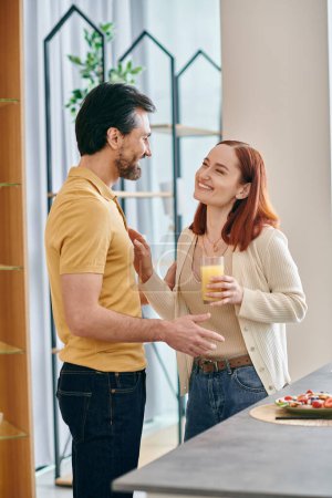 A bearded man and a redhead woman engaged in a deep conversation while standing in a modern kitchen.