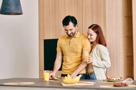 A beautiful adult couple, a redhead woman, and a bearded man, preparing breakfast in a modern apartment.
