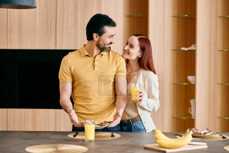 Foto de Una mujer pelirroja y un hombre barbudo de pie en una cocina llena de plátanos, pasando tiempo de calidad juntos en casa. - Imagen libre de derechos