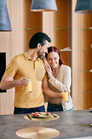 A redhead woman and bearded man stand together in front of a kitchen counter in a modern apartment.