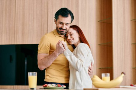 Foto de Una pelirroja y un hombre barbudo se abrazan apasionadamente en una cocina moderna, mostrando amor y unión. - Imagen libre de derechos