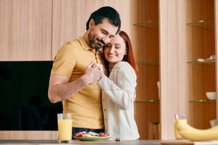 Téléchargez les photos : Une femme rousse et un homme barbu embrassant dans leur cuisine moderne, partageant un moment tendre ensemble. - en image libre de droit